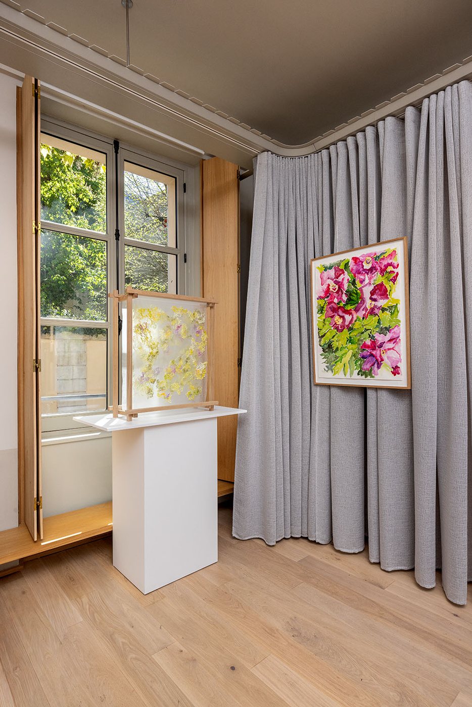 Une sculpture sur socle et une peinture florale accrochée, dans un intérieur